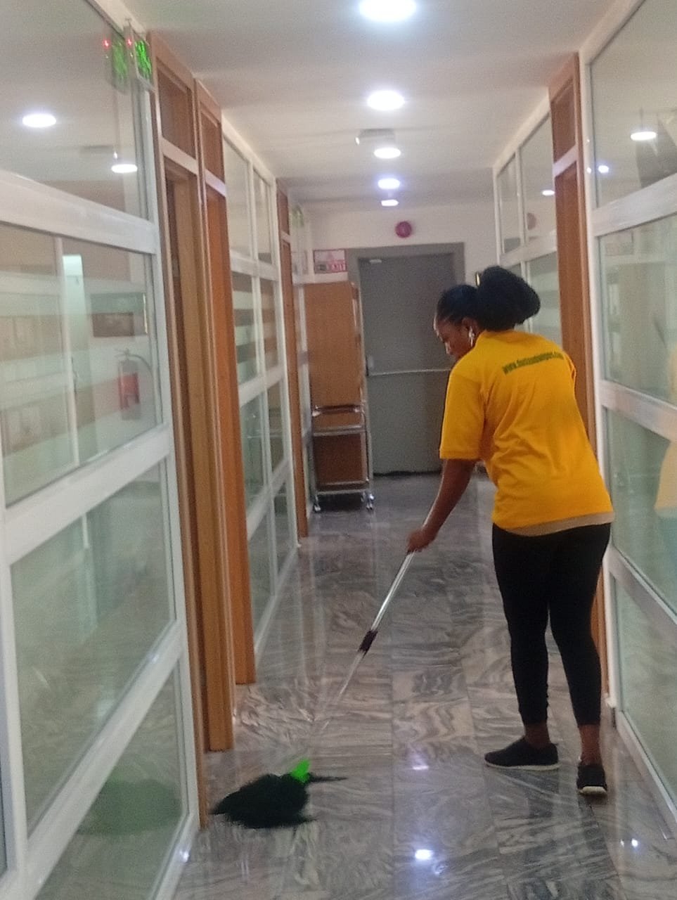 Dust and Wipes female staff sweeping a glass-wall office corridor in Abuja